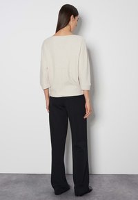 Hellbeige strukturierter Pullover mit 3/4-Ärmeln, lockerer Passform und offenem Rücken, kombiniert mit schwarzen weiten Hosen.