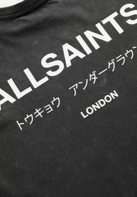 Černé bavlněné tričko s velkým bílým nápisem: "ALLSAINTS," japonskými znaky a "LONDÝN" na spodní části. Měkká, mírně strukturovaná tkanina.
