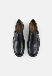 Mocassins en cuir noir avec une finition lisse, dotés d'une boucle en argent et de détails de couture subtils. Conception à bout fermé avec des bords arrondis.