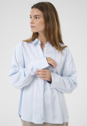 Helle blaue Button-Down-Bluse aus glattem Stoff mit lässiger Passform, langen Ärmeln und einfachen Knopfmanschetten. Auffälliger, gewölbter Saum und Kragen-Design.