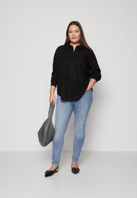 Black button-up shirt, light blue skinny jeans, gray handbag, and black flats. Smooth fabric, classic design, and fitted silhouette.