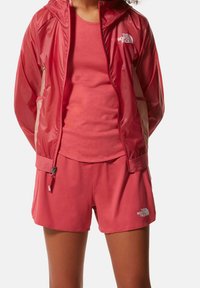 Röd lättviktsjacka med huva, ihop med en matchande linne och shorts. Har logotypdetaljer och en slät textur.