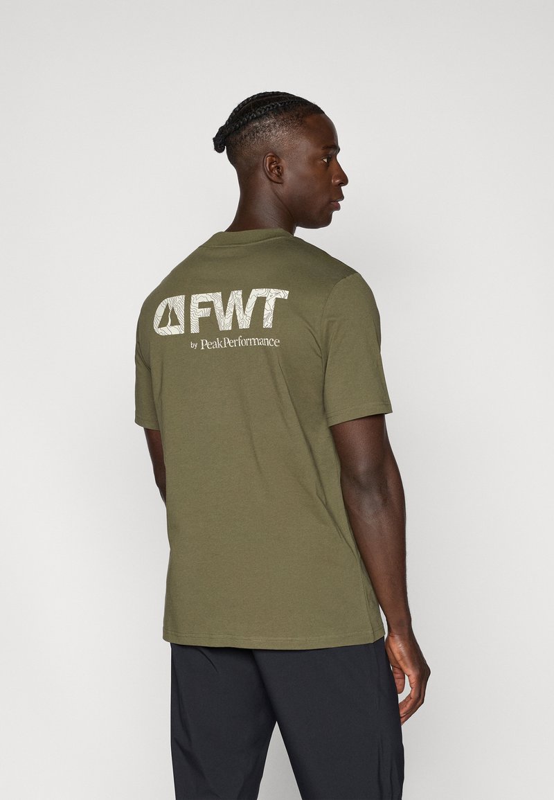 Camiseta de algodón color verde oliva, de manga corta y cuello redondo, que presenta un logo de texto blanco "FWT by PeakPerformance" en la parte posterior.
