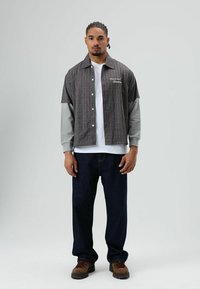 Korte mouwen, overhemd met knopen en een ruitpatroon in bruin en grijs, gecombineerd met een wit T-shirt en donkerblauwe spijkerbroek. Bruine wandelschoenen.