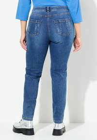 Jeans de mezclilla azul de tiro medio con una forma ajustada, que cuentan con dos bolsillos traseros y costuras sutiles. Llevados con botas de plataforma plateadas.