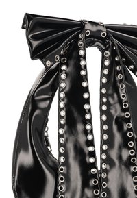 Černá kabelka z lakované kůže s designem mašle, zdobená stříbrnými průchodkami podél strany a hladkou, lesklou texturou.