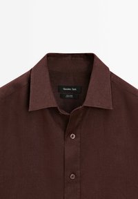 Chemise en lin brun foncé boutonnée avec col pointu et étiquette de marque Massimo Dutti à l’intérieur de l’encolure.