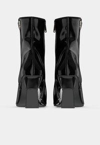 Stivali alla caviglia in pelle verniciata nera con tacco quadrato, dettagli con zip sul retro e una finitura lucida e elegante.