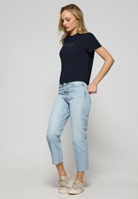 T-shirt à manches courtes navy avec "Polo Club" imprimé en fil clair, associé à un jean cropped bleu clair et des sneakers beiges.