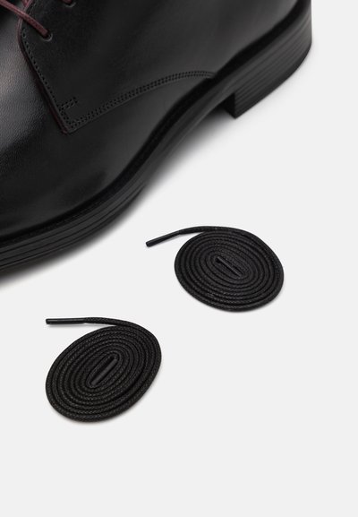 Schwarzer Lederschuh mit glatter Oberfläche und runder Zehe, kombiniert mit zwei schwarzen runden Schnürsenkeln mit Kunststoffspitzen.