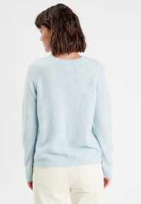 Suéter azul claro con una textura suave, puños acanalados y cuello redondo; combinado con pantalones de pana color crema.