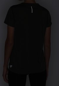 Svart atletisk T-shirt med korta ärmar, med reflektorfästen längs ryggraden och en cirkulär logotyp på nedre fållen.