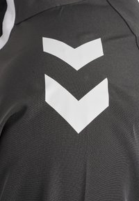 Mørkegrått stoff med en teksturert finish har to store hvite chevrondesign. Materialet ser lett og pustende ut.