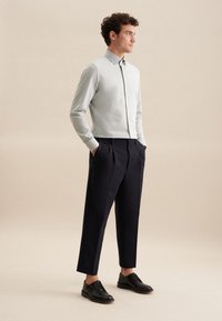 Lichtblauw, overhemd met kraag in een slim fit en verborgen knoopsluiting; gecombineerd met donkerblauwe, geplooide broek en zwarte schoenen.