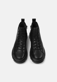 Zapatillas altas negras de cuero liso con una suela texturizada, que presentan cordones, una lengüeta con marca y detalles de cremallera en la parte trasera.