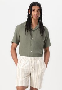 Kortærmet olivengrøn ribbet skjorte med knaplukning; parret med beige mønstrede shorts med lodrette striber og elastisk talje.