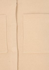 Beige tröja med en strukturerad stickad mönster, försett med två stora framfickor och en rak skärning.