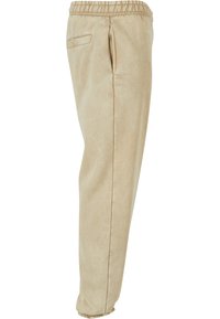 Beige joggebukser laget av myk stoff, med elastisk midje, sidelommer og elastiske mansjetter ved anklene.