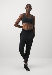  svarte joggebukser med elastisk midje og mansjetter, samt snøring. Båret sammen med en tettsittende svart ribbestrikket crop top og svarte treningssko.