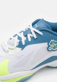 Scarpa sportiva blu e bianca realizzata in materiali mesh e sintetici, con accenti verdi e un logo circolare sul lato.