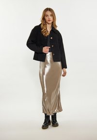 Schwarze gekürzte Jacke mit Knöpfen, langer glänzender beiger Rock und schwarze Schnürstiefel. Glatte Texturen und kontrastierende Farben.