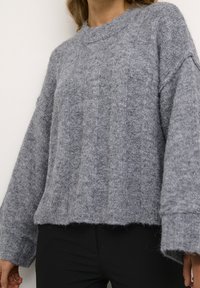 Grå stickad tröja med lös passform, med en ribbad textur och vida ärmar, tillverkad av ett mjukt, fluffigt material.