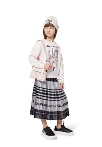 Pink sweatshirt with city graphic, black pleated skirt featuring white and black stripes, black sneakers, and beige knit beanie with logo.