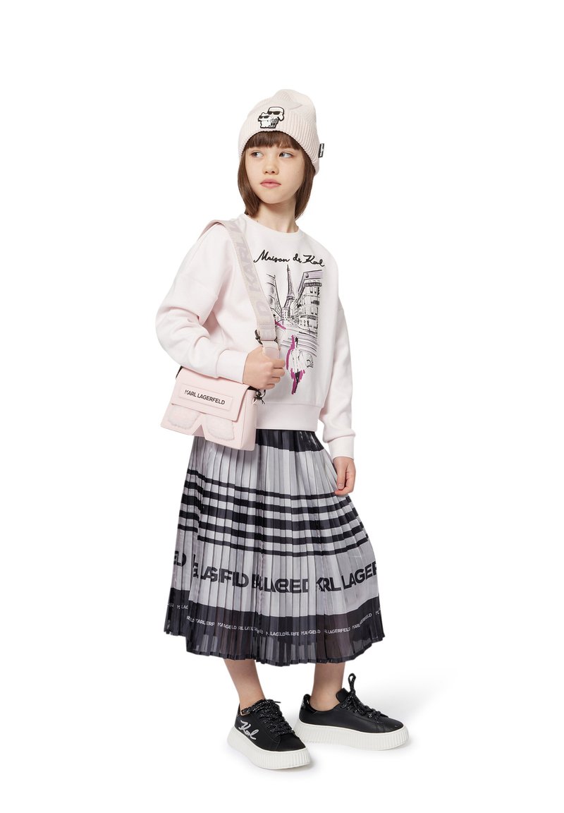 Pink sweatshirt with city graphic, black pleated skirt featuring white and black stripes, black sneakers, and beige knit beanie with logo.