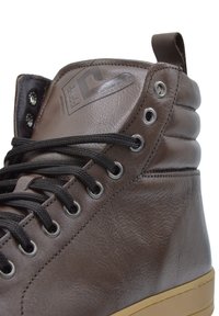 Brązowy skórzany but typu high-top z czarnymi sznurowadłami, subtelną fakturą, metalowymi oczkami i gumową podeszwą. Posiada markowy logo na języku.