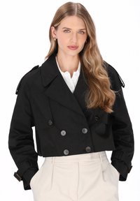 Trench coat nero corto con chiusura doppiopetto con bottoni, spalline e tasche laterali, realizzato in un tessuto liscio e strutturato.