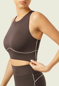 Brown sports crop top with a round neckline, featuring white accent stitching, fitted design, and smooth, stretchy fabric.