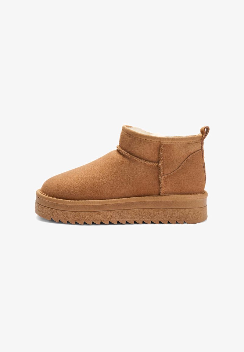 Tan ruskind ankle boot med rund tå, stikninger og kunstlæderfor. Har en tekstureret gummisål og en trækflap.