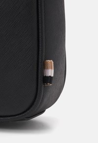 Juodas tekstūruotas maišelis su subtiliu raštu. Išskirtiniai bruožai apima mažą, dryžuotą audinio akcentą juoda, balta ir tan spalvomis.