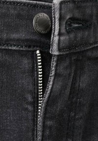 Blugii negri din denim au un nasture metalic și închidere cu fermoar, cu detalii subtile de cusături și o textură netedă.