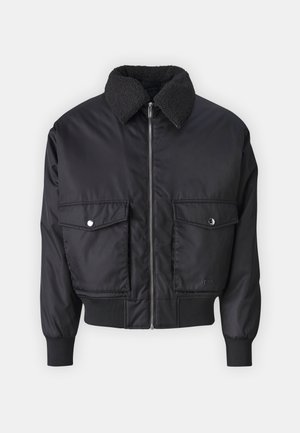 Czarna kurtka bomberka z kołnierzem z owczej wełny, zamek z przodu, dwie kieszenie z klapką, ściągacze na rękawach i u dołu oraz gładka, błyszcząca tekstura.