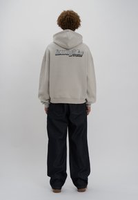 Ljusgrå luvtröja med stort svart "howdy"-tryck. Bärs över mörkblå vida jeans. Mjuk och len textur.