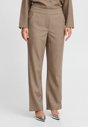 Beige weite Hose aus einem glatten Material mit elastischem Bund und seitlichen Taschen, kombiniert mit silbernen spitzen Schuhen.