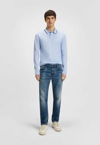 Ljusblå långärmad polo med en kontrasterande mörk krage, i kombination med blekta blå jeans och ljusa sneakers.