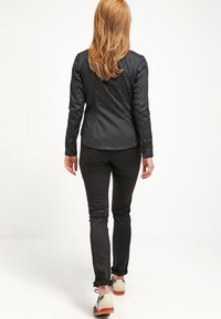 Svart, åtsittande skjorta i kombination med smala svarta byxor. Noterbara detaljer inkluderar uppkavlade ärmar och ljusa skor med röda accenter.