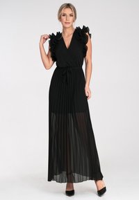 Schwarzes, plissiertes Maxikleid mit Rüschensäulen und einem gebundenen Taillengürtel. Der transparente Stoff am Rock sorgt für einen geschichteten Effekt.