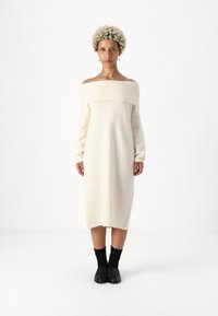 Φόρεμα με ώμους έξω, μακριά μανίκια, σε κρέμ πλέ knit ύφασμα; ίσια, μήκους midi, με ραβδωτό ντεκολτέ και μαλακή υφή; συνδυασμένο με μαύρα αξεσουάρ.