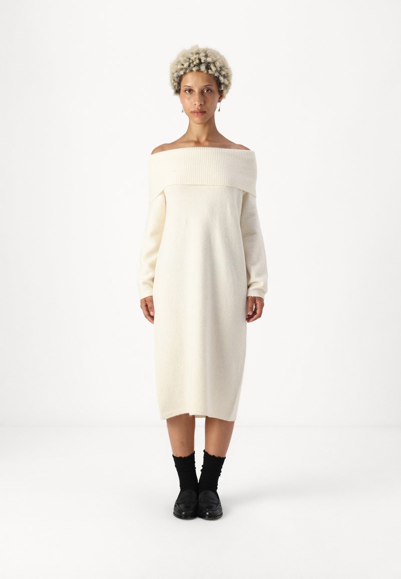 Φόρεμα με ώμους έξω, μακριά μανίκια, σε κρέμ πλέ knit ύφασμα; ίσια, μήκους midi, με ραβδωτό ντεκολτέ και μαλακή υφή; συνδυασμένο με μαύρα αξεσουάρ.