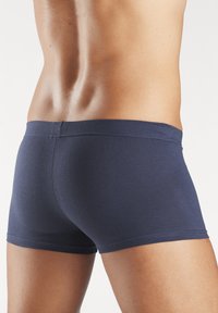 Marineblaue Baumwoll-Boxershorts mit einer engen Passform, glatter Textur und flachem Bund, seitlich gezeigt, wobei die Taille und die Bein-Nähte hervorgehoben werden.