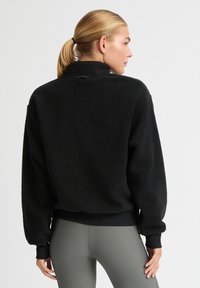 Pullover in pile nero con colletto alto, polsini e vita elasticizzati. Texture morbida con vestibilità rilassata, adatto per un abbigliamento casual.