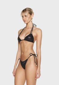 Zwarte bikini set met een driehoekige top, dunne bandjes en geplooide details op de onderkant met kraalaccenten, gemaakt van glanzende, gestructureerde stof.