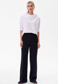 Witte, gedrapeerde top met lange mouwen en een ronde halslijn, gecombineerd met zwart, hooggewaisted, wijduitlopende broek. Minimalistisch ontwerp, gladde textuur.