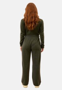 Ciemnozielony dzianinowy kombinezon z długimi rękawami, luźnym fasonem w talii i szerokimi nogawkami, wykonany z miękkiej, teksturowanej tkaniny.