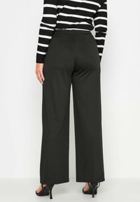 Wijd-uitlopende zwarte broek van zacht materiaal, met een hoge tailleband en een soepele textuur, gecombineerd met zwarte hoge hakken.