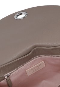 Borsa Coccinelle, esterno in morbida pelle grigia, hardware in metallo, forma strutturata, presenta un interno in tessuto rosa con una tasca con zip e etichetta del marchio.