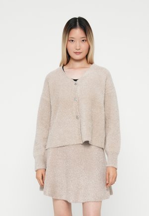 Beige fuzzy cardigan with long sleeves and a v-neck, featuring a button closure. Paired with a matching fuzzy skirt. Soft texture.